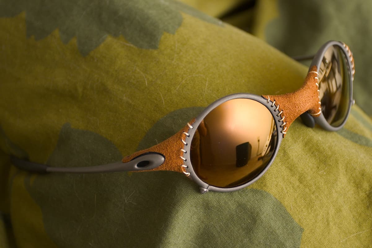 A pair of wraparound sport sunglasses with metal frame and gold iridium lenses on a plain background.