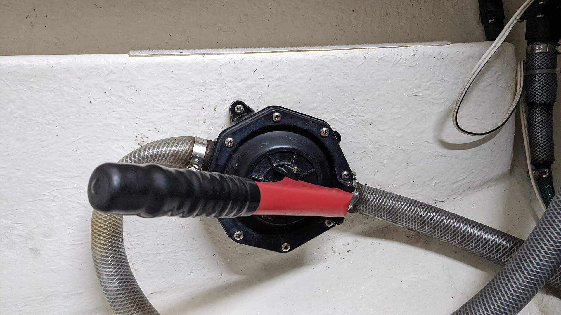 A manual diaphragm bilge pump mounted on a boat bulkhead, with handle and inlet and outlet hoses