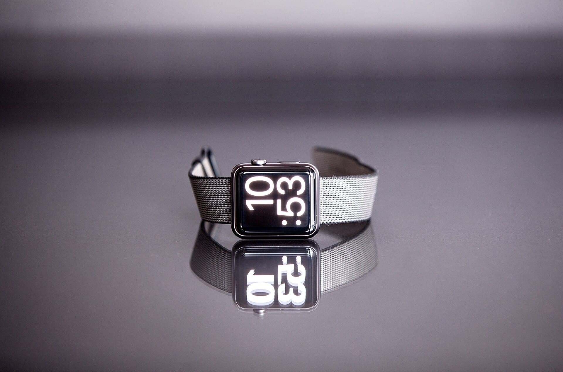 An Apple Watch resting on its side on a flat surface, the display reading 10:53